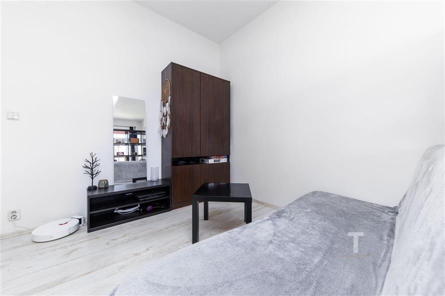 Malý obývací pokoj s moderním světlým designem, parketová podlaha, tmavá vestavěná skříň a světlý gauč přidávají stylový kontrast.