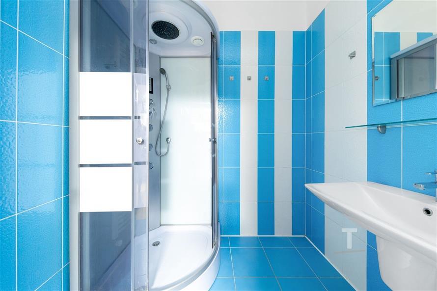 Moderní koupelna s modrou dlažbou, sprchovým koutem a závěsným umyvadlem, světlé dlaždice na stěnách, stylový a čistý design