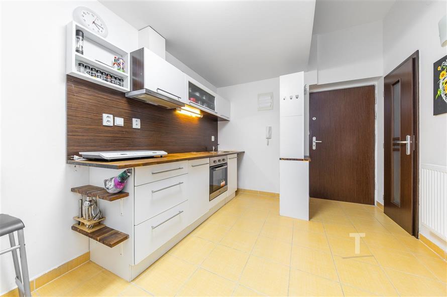 Moderní kuchyň s dřevěnou pracovní deskou, světlou dlažbou a vestavěnými spotřebiči. Skříně s elegantními úchyty nabízejí dostatek úložného prostoru.