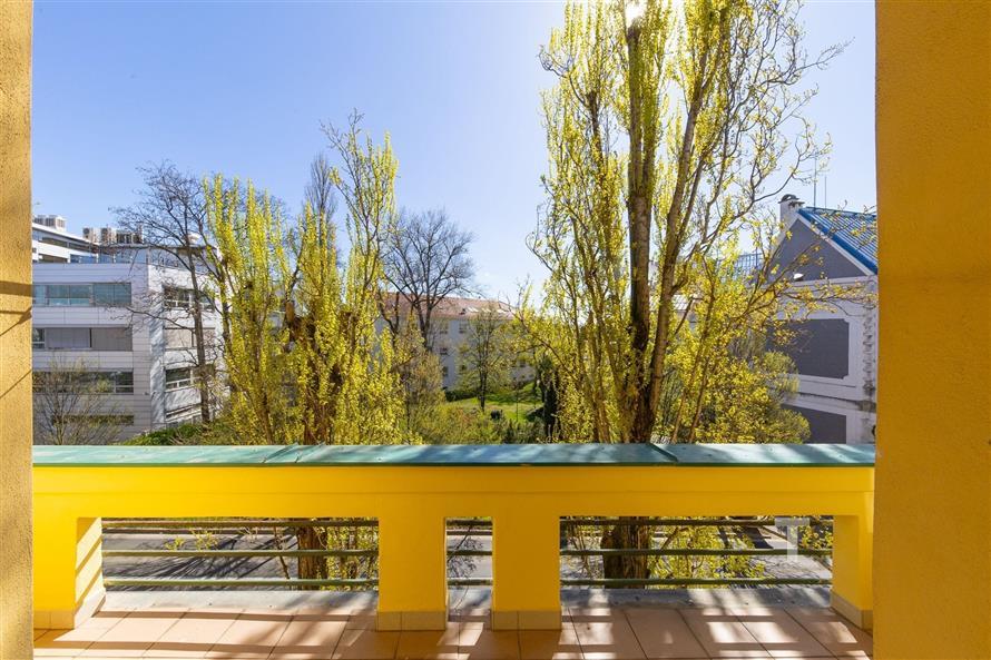 Výhled z balkonu s dlažbou, obklopený zelení a stromy, nabízí soukromí a klidnou atmosféru ve městě.