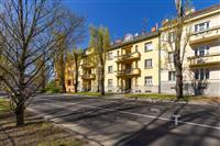 Bytový dům s rekonstruovanými balkony, nové fasády, stromy lemující ulici, slunečný den, klidná rezidenční lokalita.