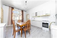 Světlá kuchyň s parketovou podlahou, vestavěnými skříněmi a moderním vybavením, velká okna poskytují dostatek přirozeného světla.