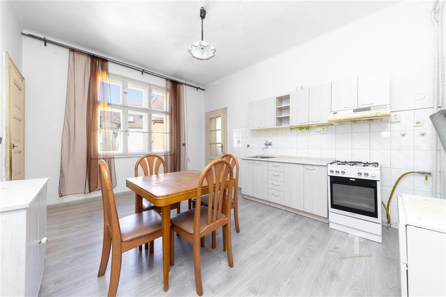 Světlá kuchyň s parketovou podlahou, vestavěnými skříněmi a moderním vybavením, velká okna poskytují dostatek přirozeného světla.