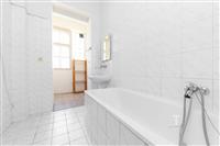 Prostorná koupelna s bílou dlažbou, světlé obklady a velké okno poskytují dostatek přirozeného světla, moderní sanita a jednoduchý design interiéru