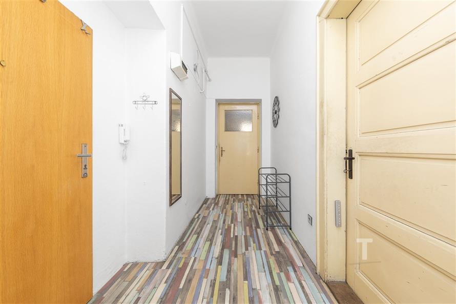 Předsíň s barevnou laminátovou podlahou, bílými stěnami a vestavěným zrcadlem, které opticky zvětšuje prostor, působí světlým dojmem.