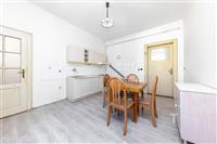 Kuchyň s dřevěnou podlahou a vestavěnými skříněmi, světlo prochází přes velká okna, místnost v rekonstruovaném stavu.