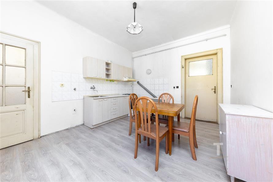 Kuchyň s dřevěnou podlahou a vestavěnými skříněmi, světlo prochází přes velká okna, místnost v rekonstruovaném stavu.