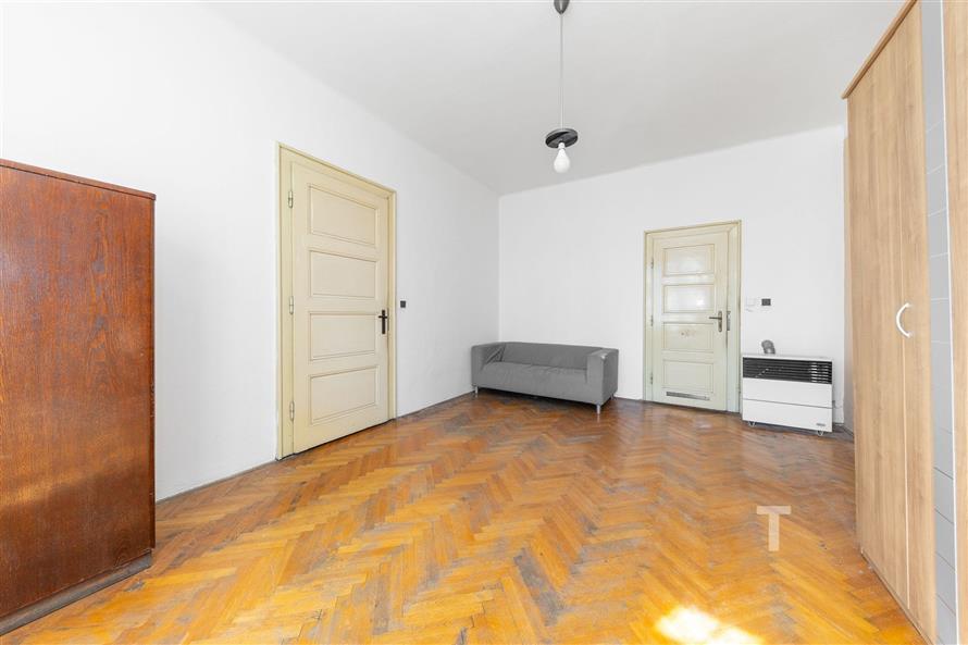 Prostorný obývací pokoj s parketovou podlahou, světlé stěny, zachovalý stav, jednoduchý nábytek, velká skříň, centrální osvětlení.