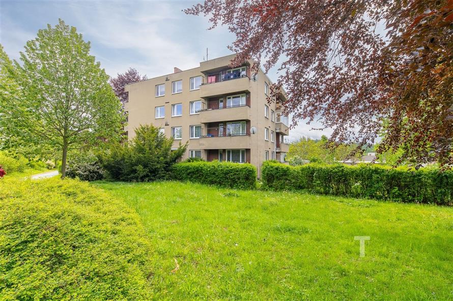 Bytový dům ve svěží zahradě s bujnou zelení a upraveným trávníkem, moderní fasáda, klidné prostředí a dobře situovaná lokalita.
