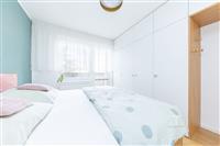 Světlá ložnice se vestavěnými skříněmi, parketovou podlahou a moderním designem, s velkými okny pro dostatek přirozeného světla.