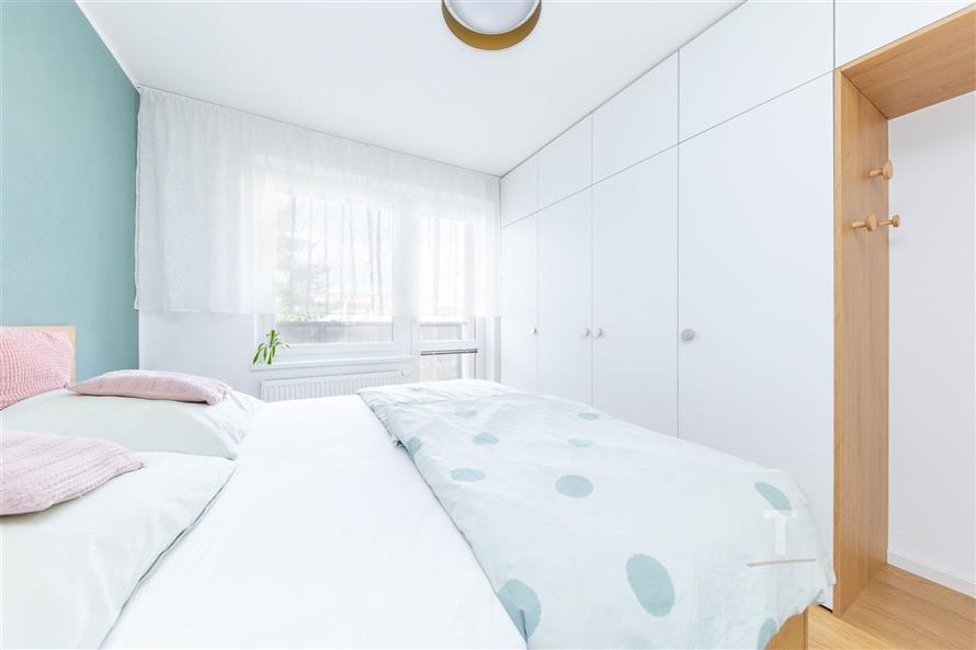 Světlá ložnice se vestavěnými skříněmi, parketovou podlahou a moderním designem, s velkými okny pro dostatek přirozeného světla.