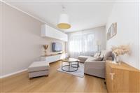 Světlý obývací pokoj s parketovou podlahou, moderní nábytkem a velkými okny, které zajišťují dostatek přirozeného světla.