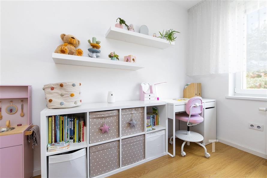 Dětský pokoj s parketovou podlahou, bílým nábytkem a dekoracemi, světlo procházející velkými okny, moderní a světlý interiér.