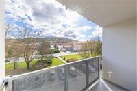 Výhled z prostorného balkonu s moderním kovovým zábradlím v klidné rezidenční oblasti, ideální pro relaxaci a venkovní posezení.