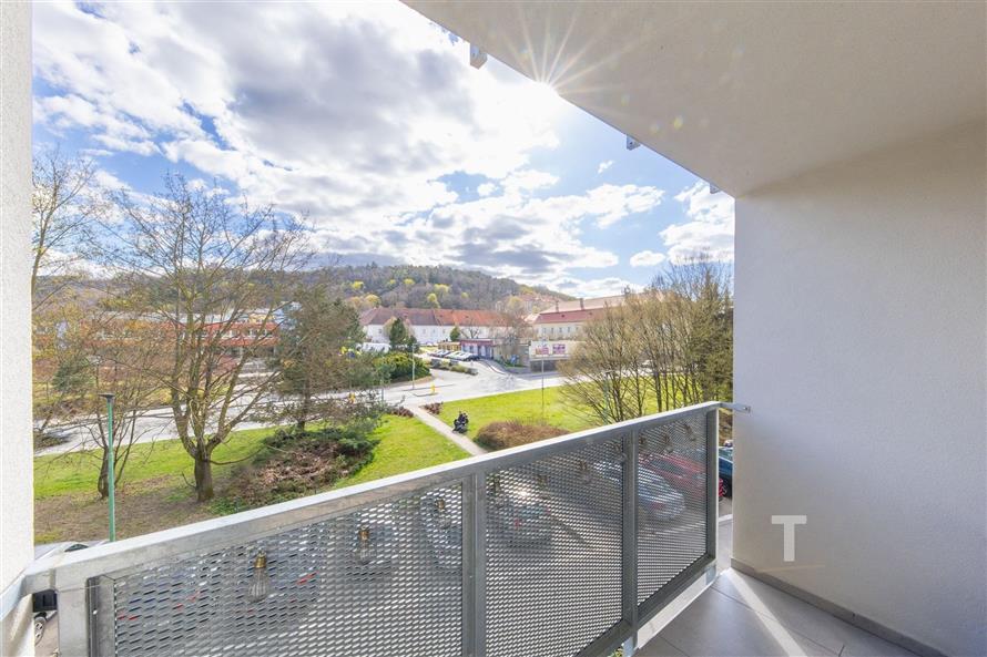 Výhled z prostorného balkonu s moderním kovovým zábradlím v klidné rezidenční oblasti, ideální pro relaxaci a venkovní posezení.