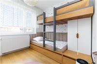 Dětský pokoj s parketovou podlahou, vestavěným nábytkem a palandou. Světlé prostředí s velkými okny a moderním dekorem.