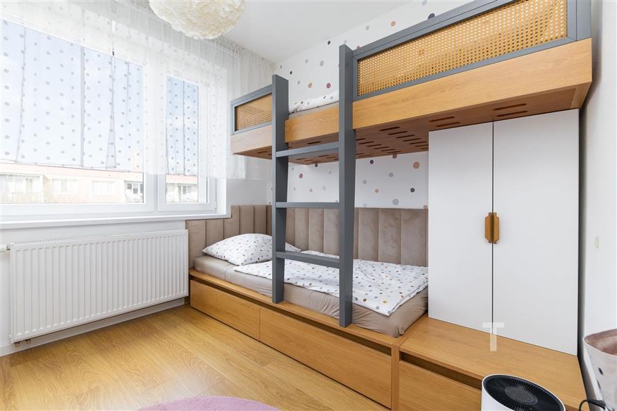 Dětský pokoj s parketovou podlahou, vestavěným nábytkem a palandou. Světlé prostředí s velkými okny a moderním dekorem.