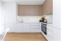 Moderní kuchyň s bílými skříňkami, dřevěnou podlahou a vestavěnými spotřebiči. Světlý prostor s elegantním designem.