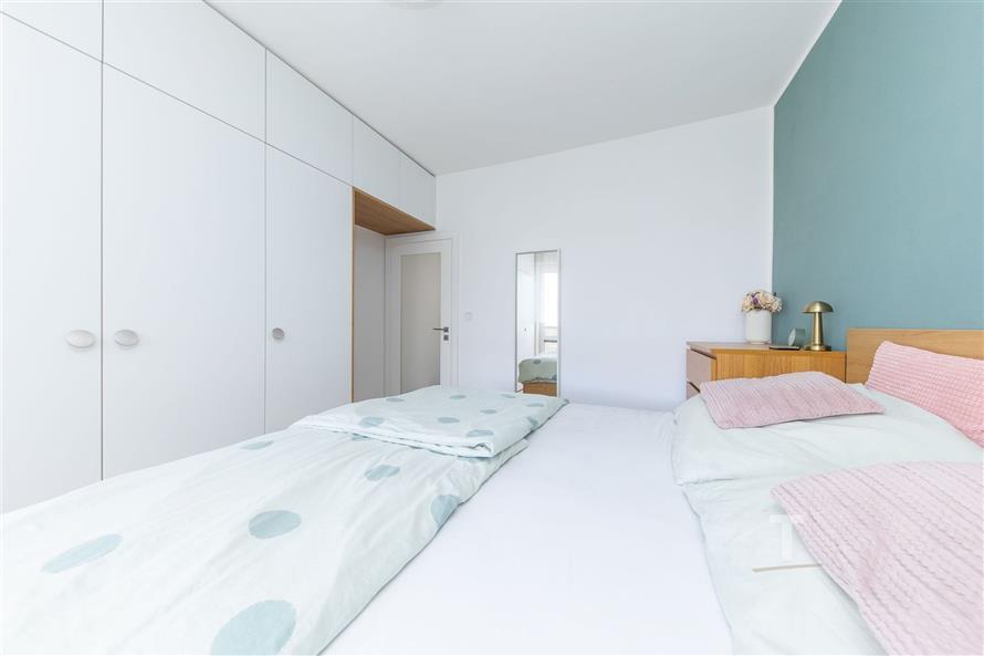 Světlá ložnice s vestavěnými skříněmi a dřevěným nábytkem, moderní styl a pastelové barvy dodávají prostoru útulnost a eleganci.