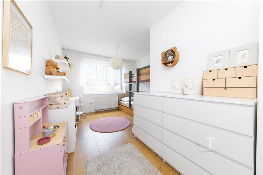 Dětský pokoj s parketovou podlahou, světlým nábytkem a velkými okny, moderní styl s palandou a úložným prostorem.