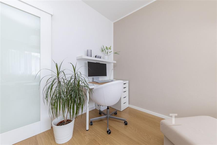 Moderní pracovní kout s parketovou podlahou, světlé stěny, vestavěné úložné prostory, minimalistický designový kancelářský nábytek.