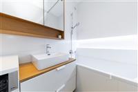 Moderní koupelna s bílými obklady, stylovým umyvadlem na dřevěné desce a vestavěným sprchovým koutem. Světlé čisté provedení.