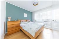 Prostorná ložnice s moderním designem, dřevěná podlaha, velká okna pro přirozené světlo, vestavěné skříně pro úložný prostor.