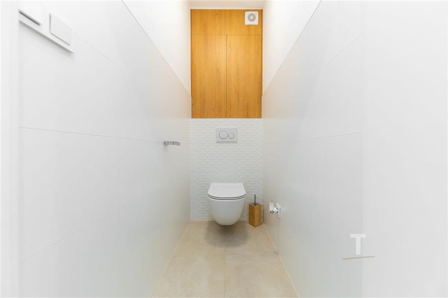 Úzká moderní toaleta s bílými dlaždicemi, dřevěný panel, minimalistický design, světlý interiér
