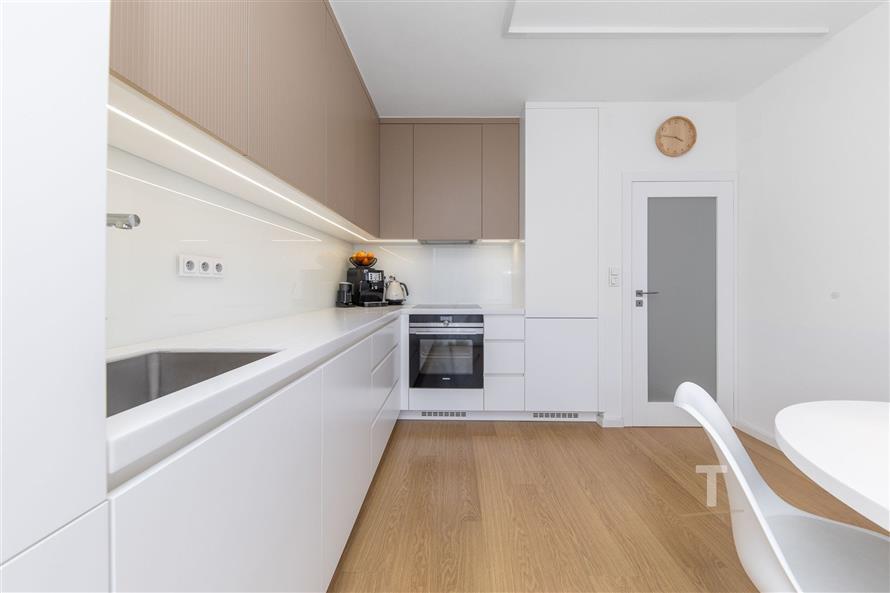 Moderní kuchyň s parketovou podlahou, vestavěnými skříněmi a světlým nábytkem, poskytuje elegantní a funkční prostor.