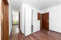 Prostorná předsíň s plovoucí podlahou, moderní vestavěné skříně a dřevěné dveře vytvářejí elegantní a funkční vstupní prostor.