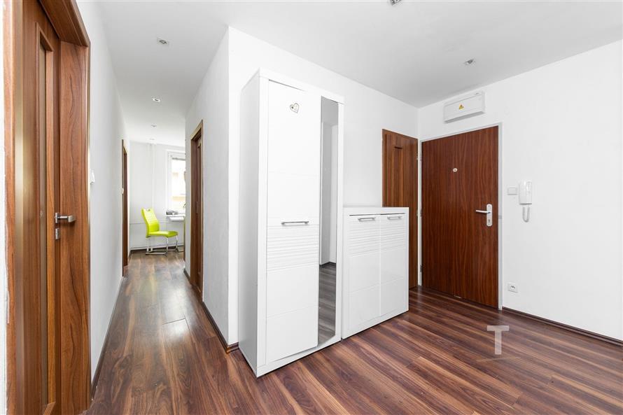 Prostorná předsíň s plovoucí podlahou, moderní vestavěné skříně a dřevěné dveře vytvářejí elegantní a funkční vstupní prostor.