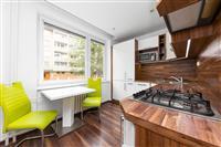 Moderní kuchyň s parketovou podlahou, dřevěnou pracovní deskou a velkými okny. Světlý prostor s vestavěnými spotřebiči a jídelním koutem.