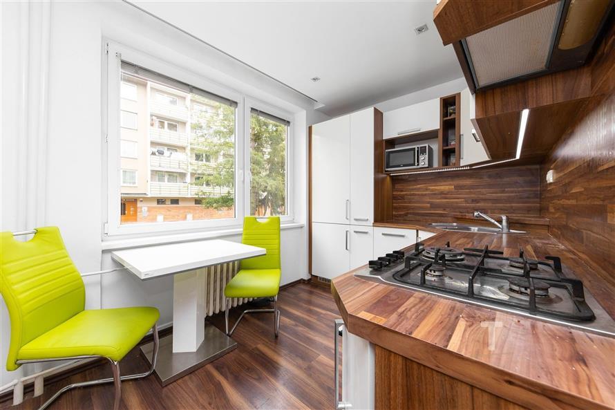 Moderní kuchyň s parketovou podlahou, dřevěnou pracovní deskou a velkými okny. Světlý prostor s vestavěnými spotřebiči a jídelním koutem.