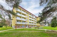 Čtyřpatrový panelový bytový dům s balkony, obklopen zelení, ideální pro klidné bydlení v rezidenční čtvrti, poblíž parků a služeb.