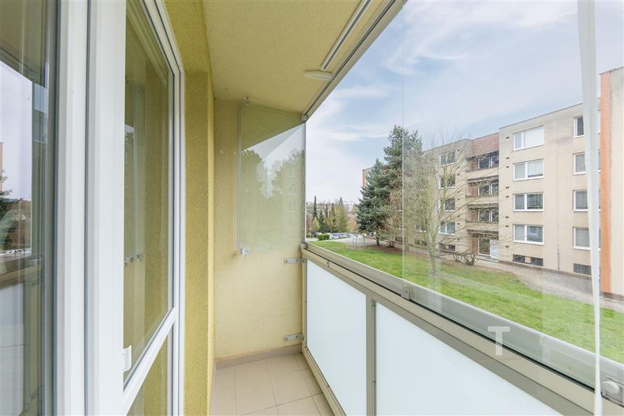 Zasklený balkon s dlažbou, moderní úprava, výhled na okolní zástavbu a zeleň, ideální pro relaxaci.