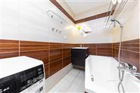 Moderní koupelna s dlažbou, dřevěnými obklady a vanou. Disponuje vestavěným umyvadlem a je vybavena moderními spotřebiči.