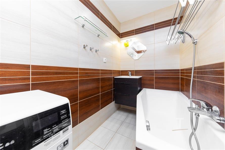 Moderní koupelna s dlažbou, dřevěnými obklady a vanou. Disponuje vestavěným umyvadlem a je vybavena moderními spotřebiči.