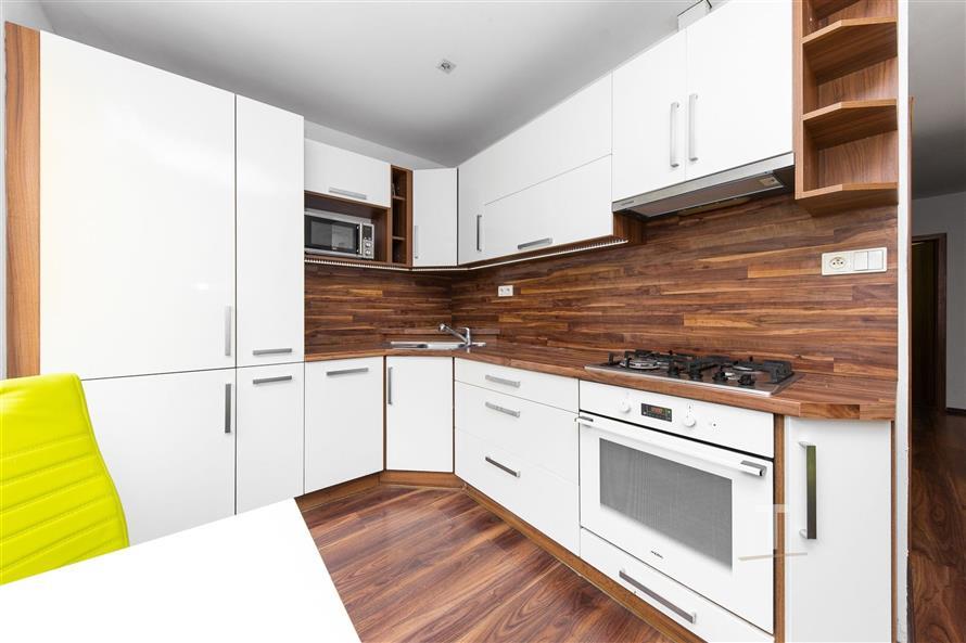 Moderní kuchyň s dřevěnou pracovní deskou, vestavěnými spotřebiči a bílými skříňkami. Parketová podlaha dodává prostoru elegantní vzhled.