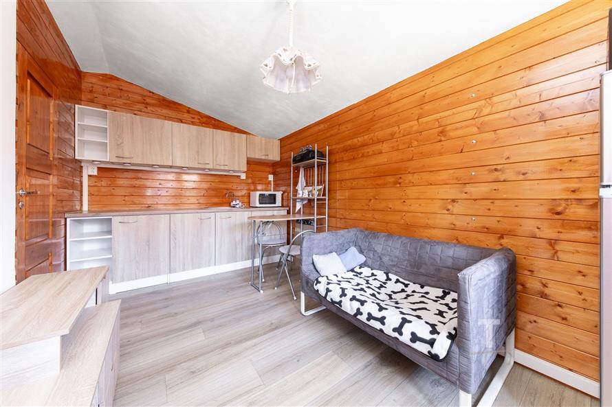 Kuchyňský kout s dřevěným obložením, moderními spotřebiči a dřevěnou podlahou, vedle které je pohodlná sedačka.
