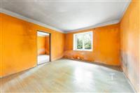 Prázdný pokoj s oranžovými stěnami, světlé parketové podlaze a velkým oknem nabízí potenciál pro rekonstruovaný interiér.