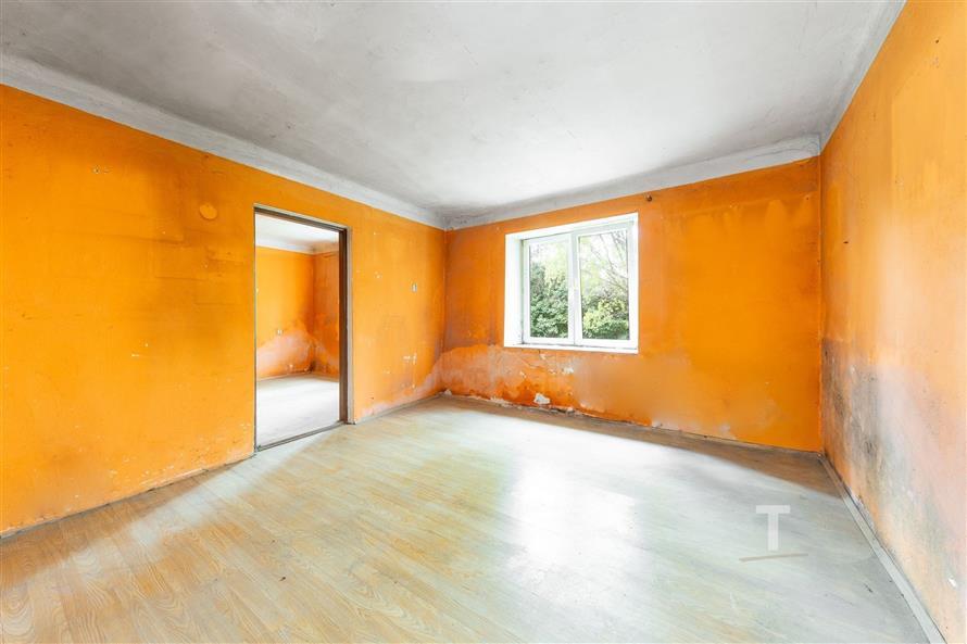 Prázdný pokoj s oranžovými stěnami, světlé parketové podlaze a velkým oknem nabízí potenciál pro rekonstruovaný interiér.
