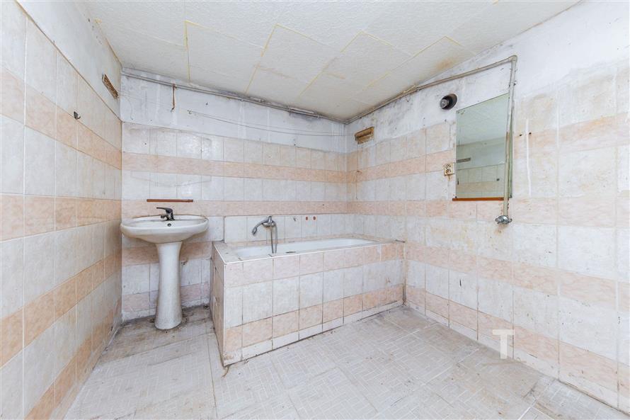 Koupelna s dlažbou, vanou a umyvadlem vyžaduje rekonstrukci, základní zařízení a starší styl nabízí potenciál pro modernizaci.