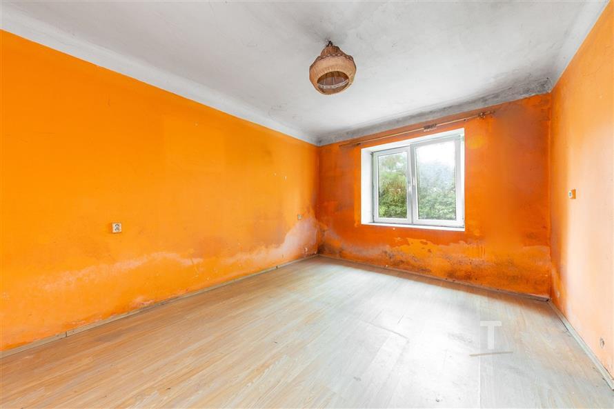 Prázdný pokoj s velkým oknem, laminátová podlaha, výrazné oranžové stěny, potřebuje renovaci, přírodní světlo.