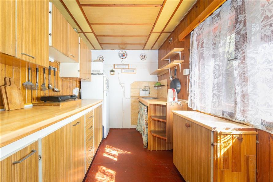 Úzká kuchyň s dřevěným obložením, světlé skříňky a velká okna s krajkovými záclonami, poskytující dostatek přirozeného světla.