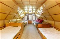 Podkrovní ložnice s dřevěnými obklady, třemi lůžky a jednoduchými okny, ideální pro rekreační účely, útulný a rustikální styl.