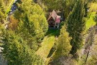 Malebná chata obklopená přírodou se šikmou střechou a dřevěnými prvky, zasazená do klidného zalesněného prostředí, ideální pro rekreaci.