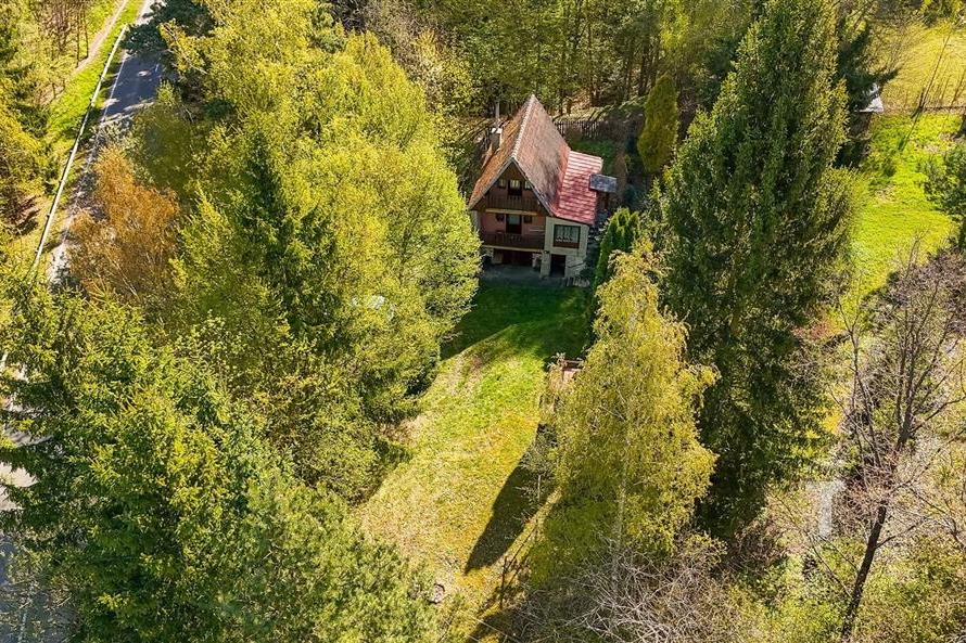 Malebná chata obklopená přírodou se šikmou střechou a dřevěnými prvky, zasazená do klidného zalesněného prostředí, ideální pro rekreaci.