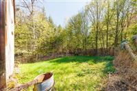 Zahrada s trávníkem a dřevěným plotem, obklopená vzrostlými stromy, nabízí soukromí a klidné prostředí pro relaxaci.