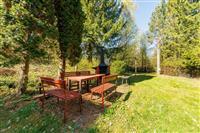 Zahrada s dřevěným nábytkem, venkovní krb a zelený trávník, obklopená vzrostlými stromy, ideální pro relaxaci a grilování venku.