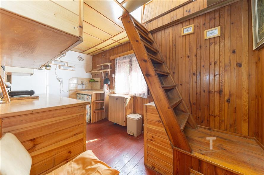 Dřevěný interiér se schody, dřevěné obložení stěn, vestavěné skříně, světlý prostor díky velkému oknu, rustikální styl.